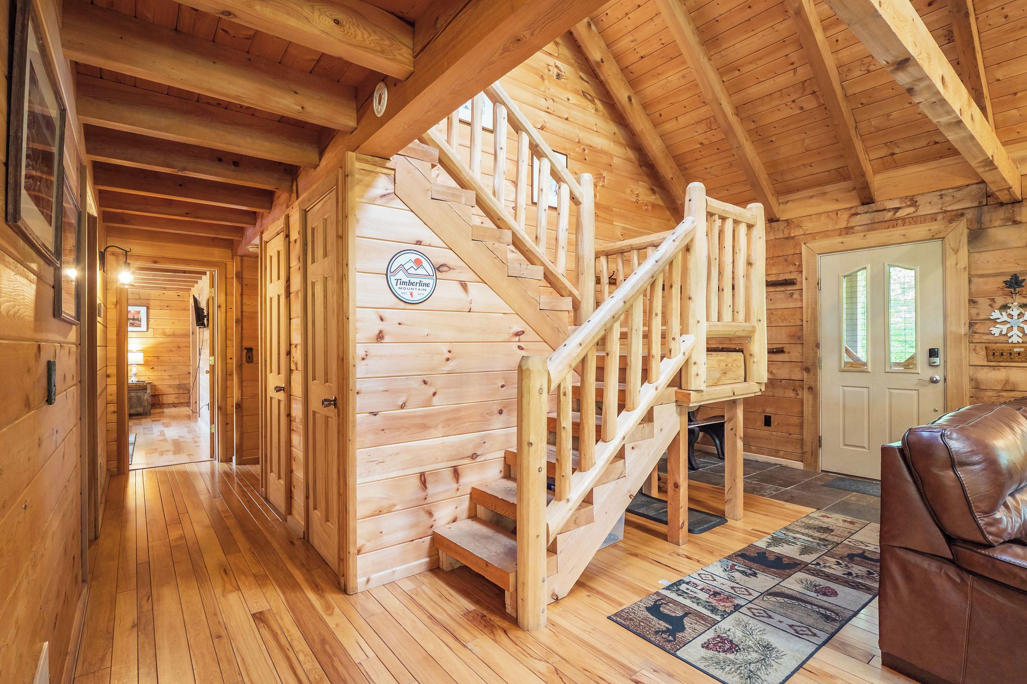 A wooden interior with a staircase leading to a loft area, a door with a snowflake decoration, and a leather sofa.