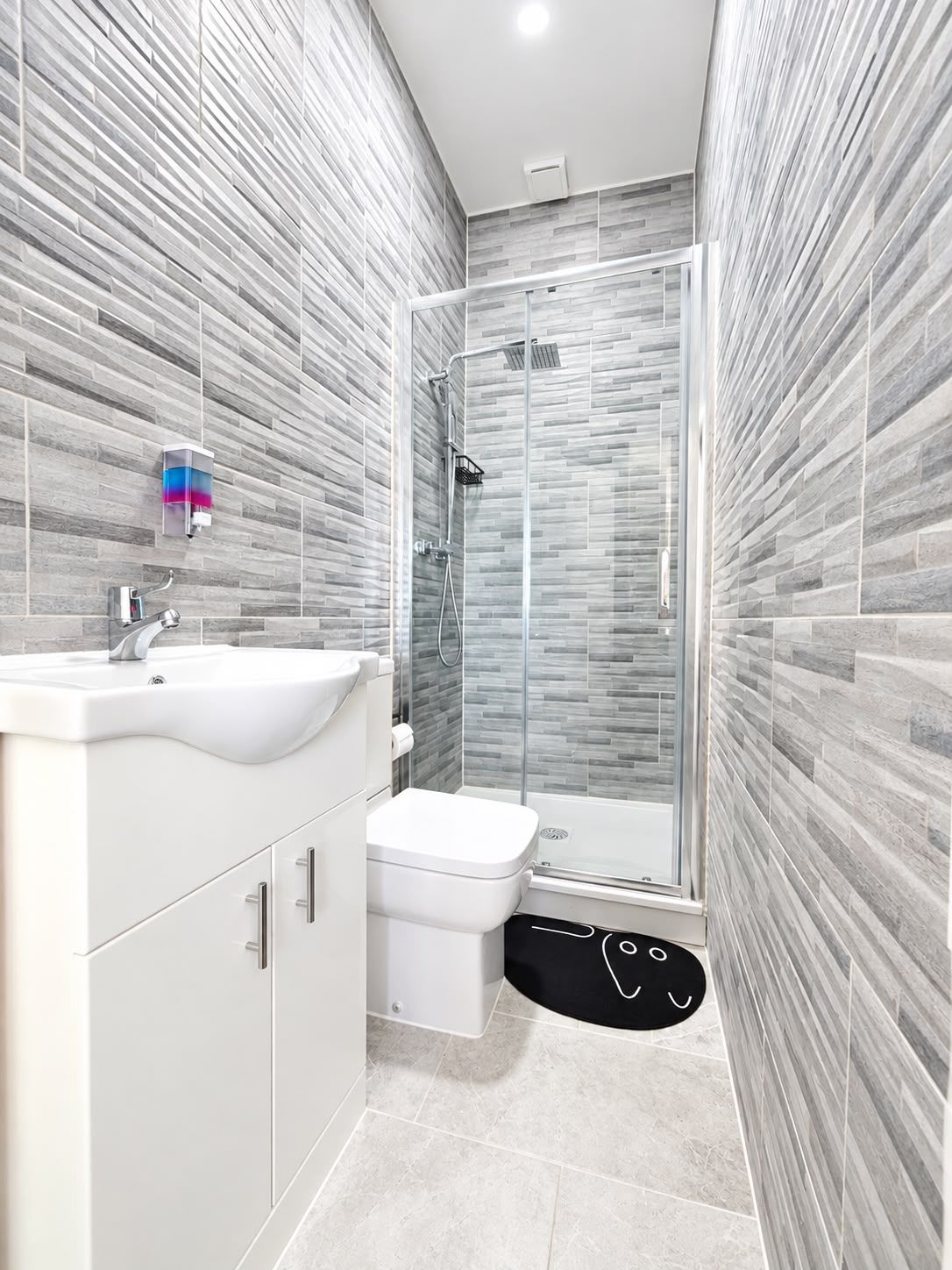A modern bathroom with a glass shower enclosure, a white sink, and a toilet.