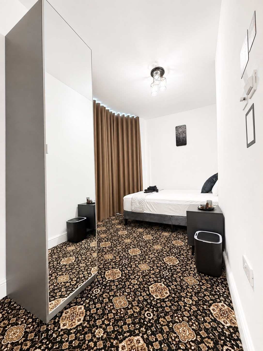 Una habitación de hotel moderna con una cama, mesitas de noche, un armario y una alfombra estampada.