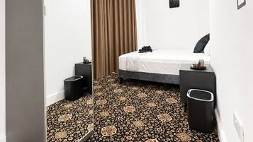 Una habitación de hotel moderna con una cama, mesitas de noche, un armario y una alfombra estampada.