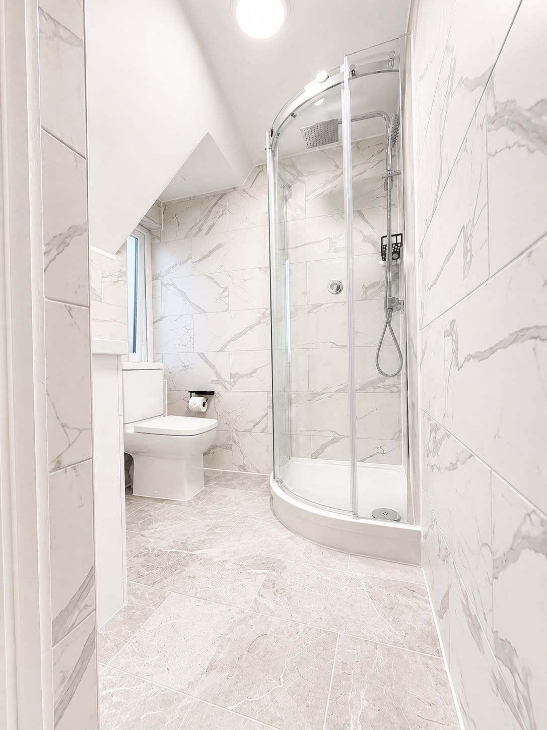 A modern bathroom with a glass-enclosed shower, a toilet, and marble flooring.