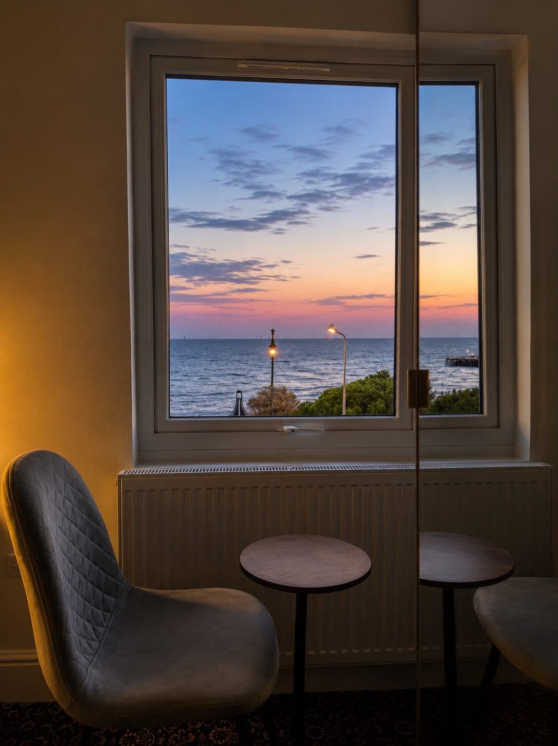 A room with a large window overlooking the sea, two small round tables, and a single chair.