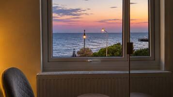 A room with a large window overlooking the sea, two small round tables, and a single chair.