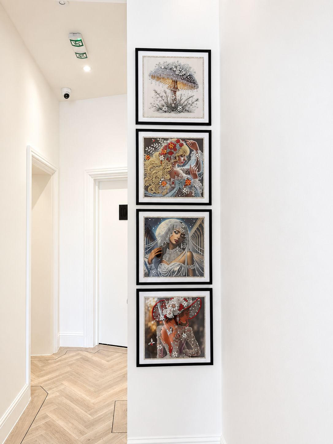 A hallway with a series of framed artworks on the wall, a white door, and a herringbone patterned floor.