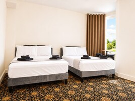 A hotel room with two beds, a window with curtains, a small table, and a patterned carpet.