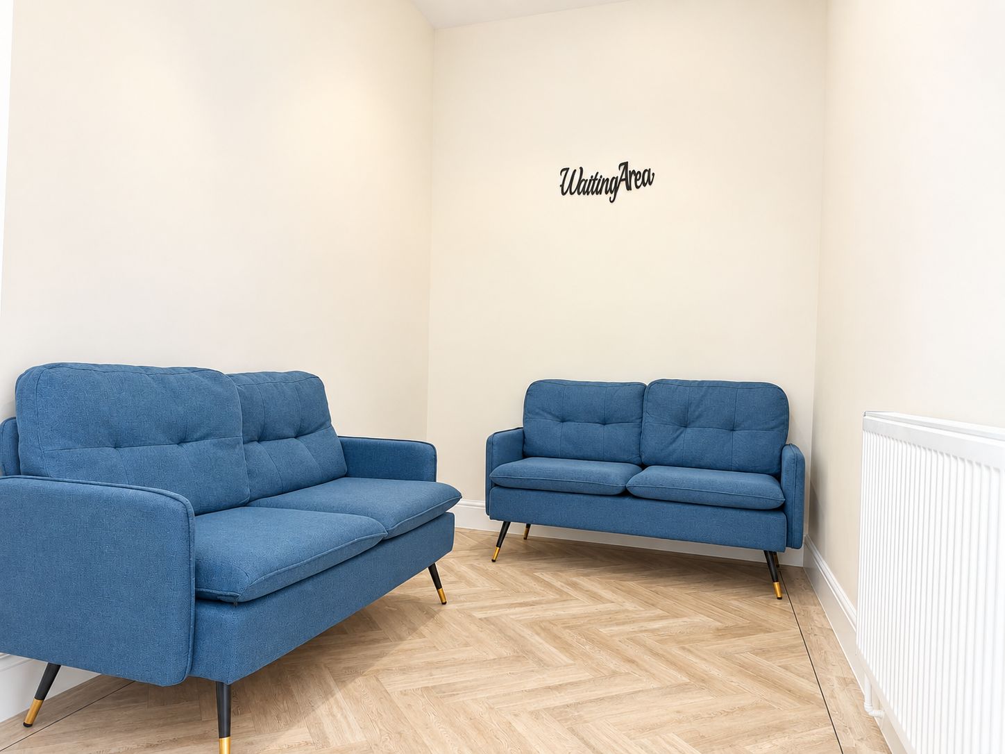Una habitación con dos sofás azules y un cartel en la pared que dice 'Waiting Area'.