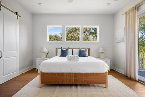 Une chambre à coucher avec un lit en bois, des murs blancs et une grande fenêtre donnant sur les arbres.