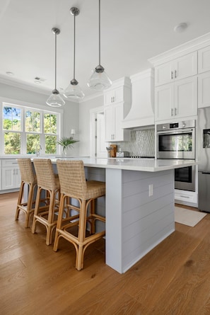 A modern kitchen with white cabinetry, a central island, and a built-in oven. - The Marsh On Broadway Walk To Shem Creek Sleeps 16 (Mt Pleasant)
