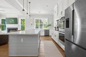 Une cuisine moderne dotée d’un grand îlot central, d’appareils électroménagers en acier inoxydable et offrant une vue sur la verdure environnante.