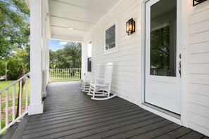 Eine überdachte Veranda mit Geländer, zwei Schaukelstühlen und einer Tür mit Fenster.