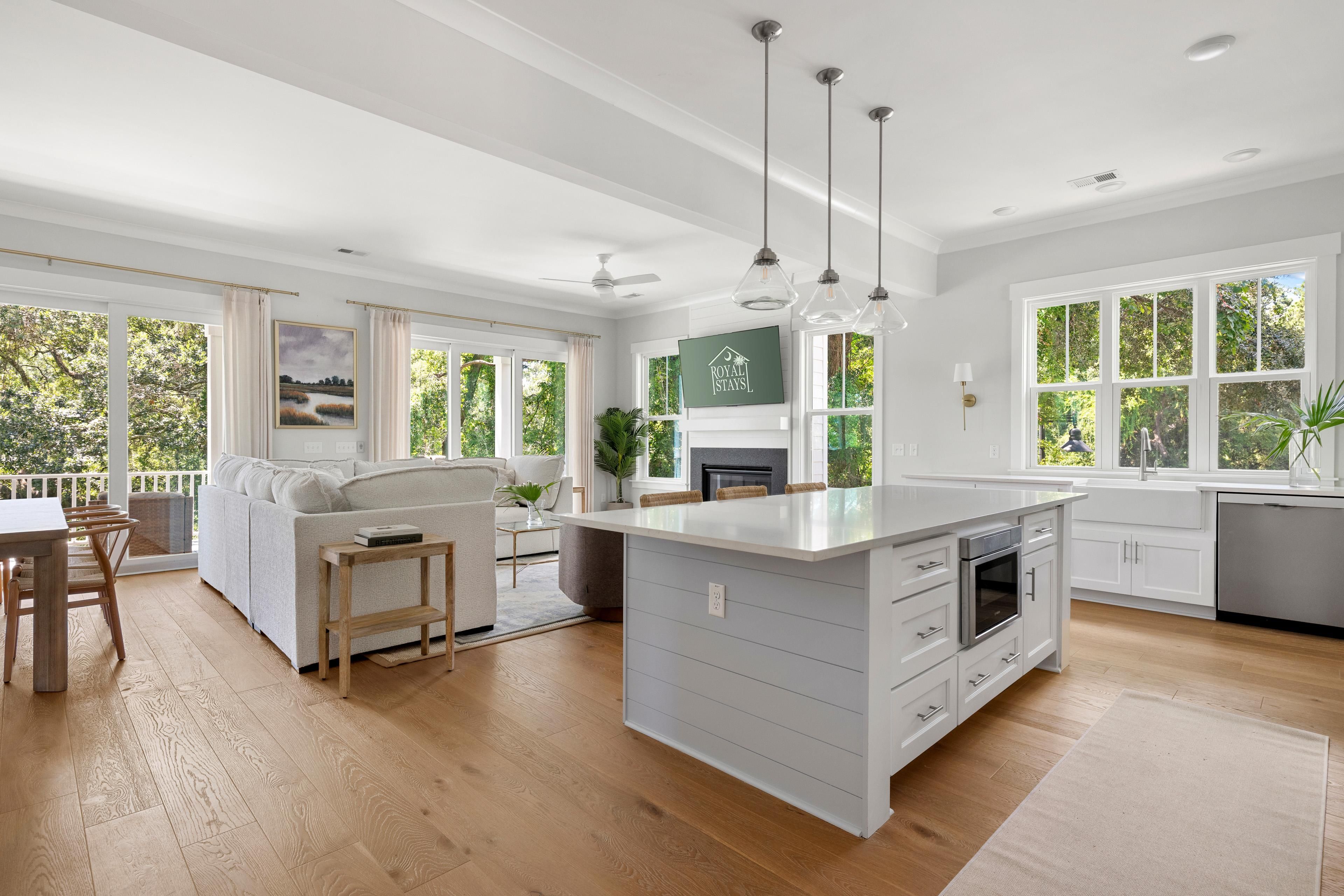 A spacious kitchen with a large island, wooden flooring, and a view of greenery outside.