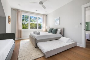Una camera da letto moderna con un letto grande, un letto più piccolo, una ventola a soffitto e vista sul verde dalla finestra.