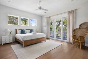 A bedroom with a bed, nightstands, a ceiling fan, a large window, and a view of the outdoors. - The Marsh On Broadway Walk To Shem Creek Sleeps 16 (Mt Pleasant)