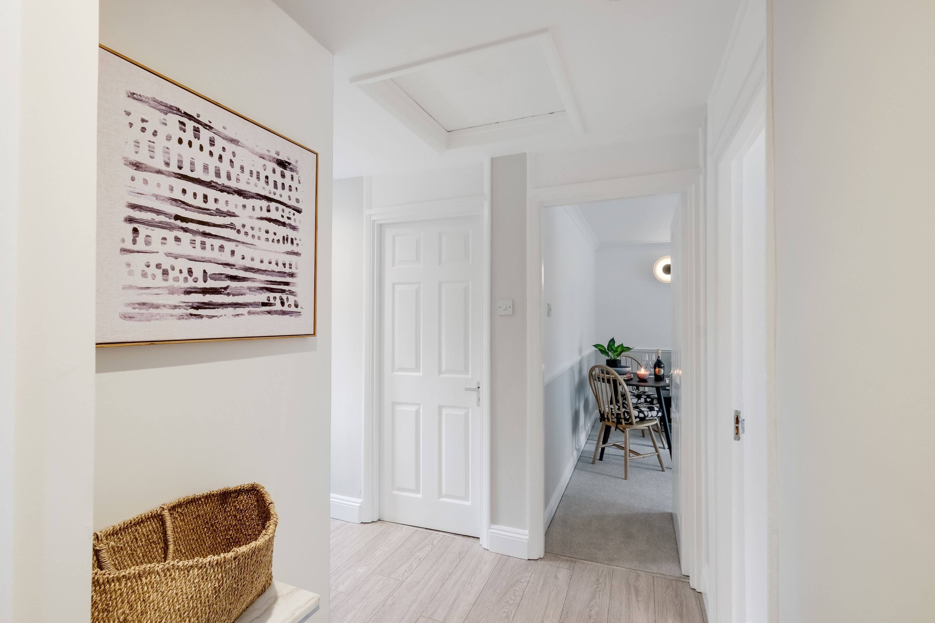 A hallway with a white door, a woven basket, and a framed artwork on the wall.
