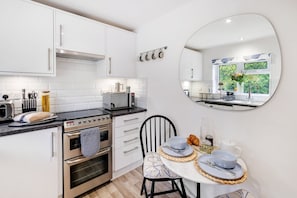 A modern kitchen with white cabinetry, a built-in oven, a microwave, and a dining area with a round table and chairs. - Modern 1-bed-Parking-Garden-Nr Warner Bros (Watford)