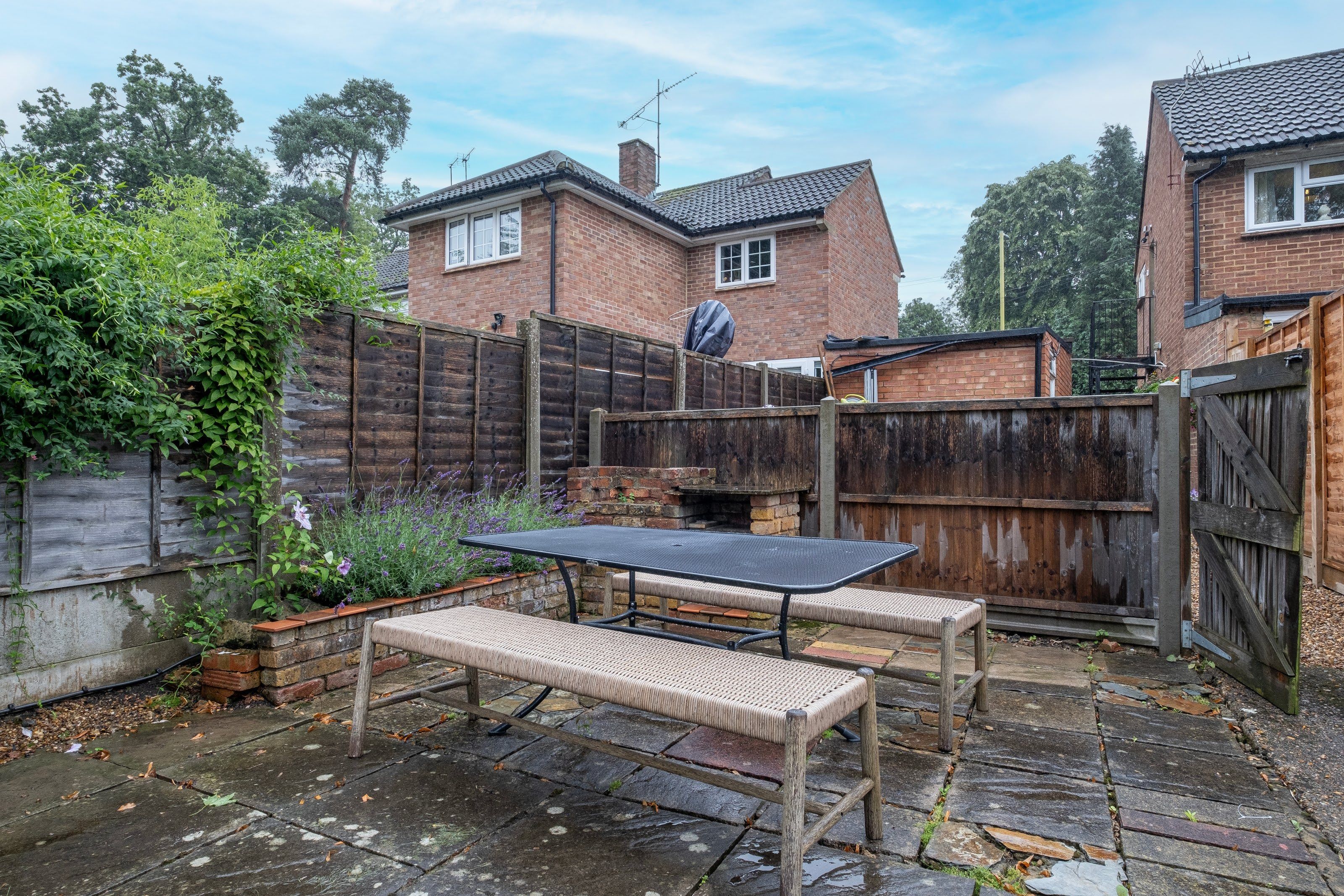 Un espace patio aménagé avec une table et des bancs, entouré d’une clôture en bois et d’un mur en briques.