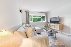 Ein modernes Wohnzimmer mit einer Couch, einem Couchtisch, einem Fernseher und einem Fenster mit Vorhängen.