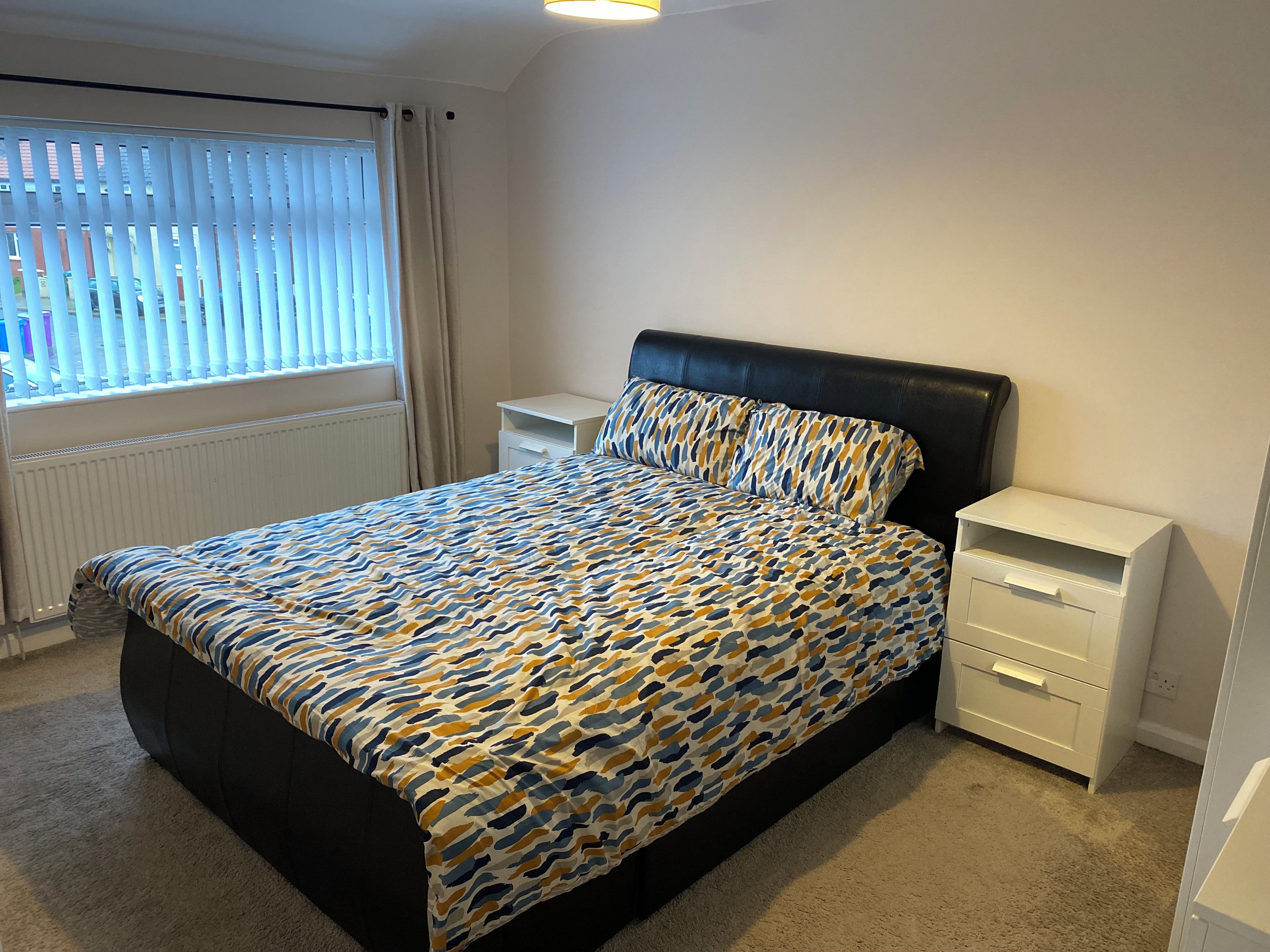 A bedroom with a bed, a nightstand, a dresser, and a window with blinds.