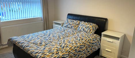 A bedroom with a bed, a nightstand, a dresser, and a window with blinds.