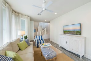 Ein Wohnzimmer mit einer Couch, einem Couchtisch, einem Fernseher auf einem weißen Schrank und einer Treppe, die zu einer oberen Ebene führt.