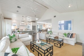 Ein geräumiges Wohnzimmer mit hohen Decken, weißen Wänden und einem großen Fenster. Zwei Sofas, ein Couchtisch und ein Essbereich sind zu sehen, im Hintergrund befindet sich eine Küche.