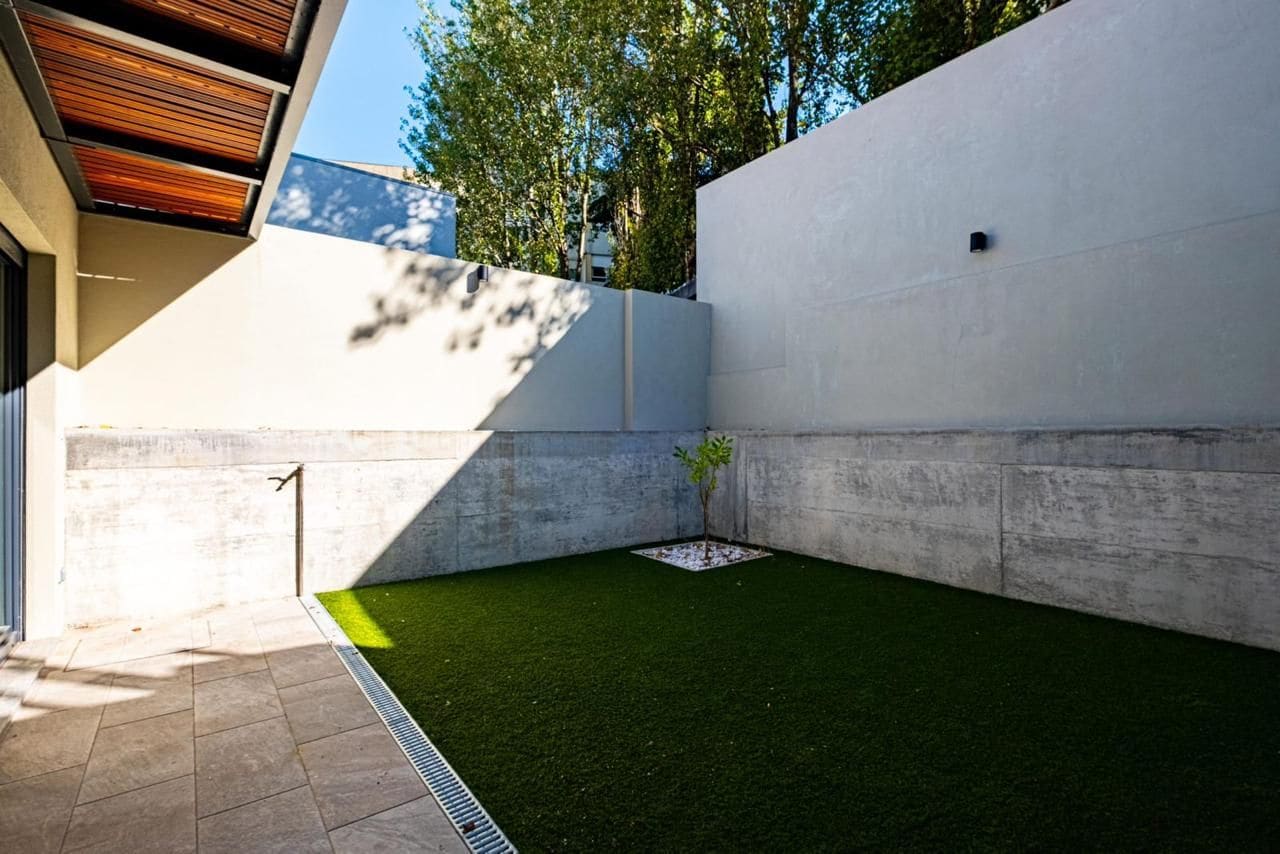 A modern outdoor space with artificial grass, a small tree, and a concrete wall.