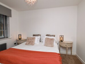 Ein Schlafzimmer mit einem Bett, zwei Nachttischen, einem Heizkörper und einem Fenster mit Jalousien.