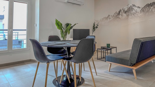 A modern dining area with a round table, chairs, a sofa, and a wall-mounted air conditioner. - #IO | Le Victoria 12 💟 (Grenoble)
