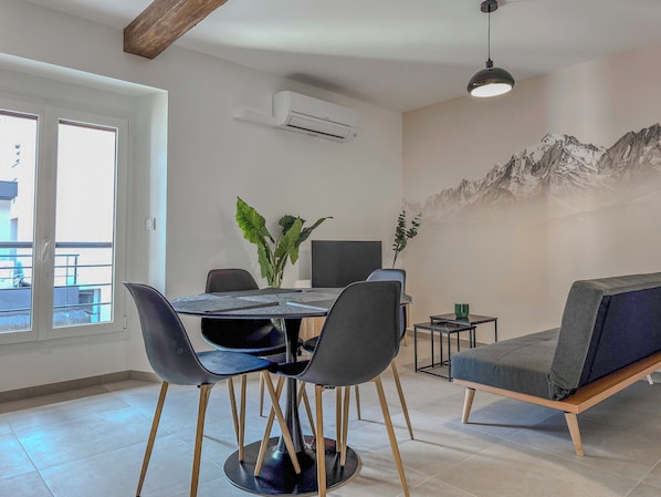 Een moderne eethoek met een ronde tafel, stoelen, een bank en een wandairconditioner.