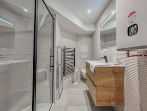 Een moderne badkamer met een glazen douchecabine, een houten wastafelmeubel en een handdoekrek.