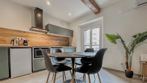 A modern kitchen with a dining area, featuring a wooden ceiling, a large window, and a potted plant. - #IO | Le Victoria 12 💟 (Grenoble)