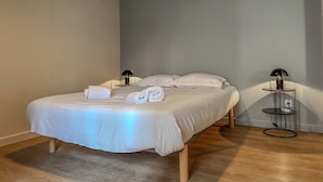 A neatly made bed with white linens and towels, a bedside table with a lamp, and a small round table with a lamp. - #IO | Le Victoria 12 💟 (Grenoble)