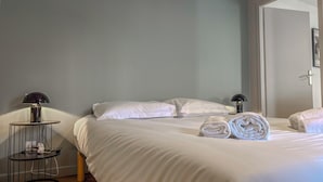 A hotel room with a bed, two bedside lamps, a round table with a lamp, and towels on the bed. - #IO | Le Victoria 12 💟 (Grenoble)
