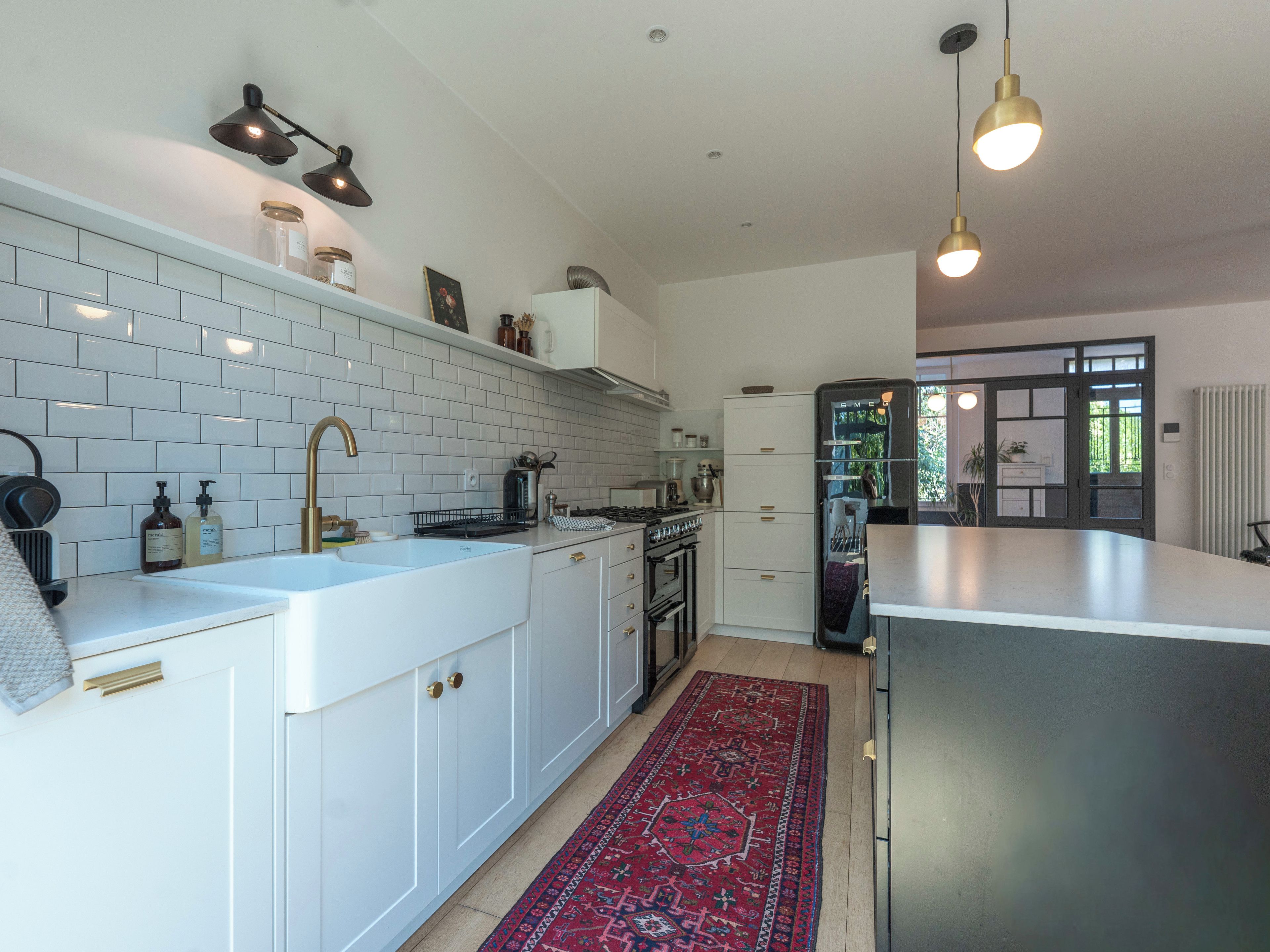 Une cuisine moderne avec des meubles blancs, un îlot central et un tapis à motifs rouges.