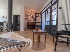 Een moderne woonkamer met een piano, een ronde tafel met decoratieve objecten, een zachte fauteuil en uitzicht door een groot raam.