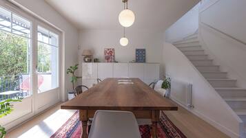 Un espace de salle à manger moderne avec une table en bois, des chaises blanches, un luminaire suspendu et une vue sur un escalier.