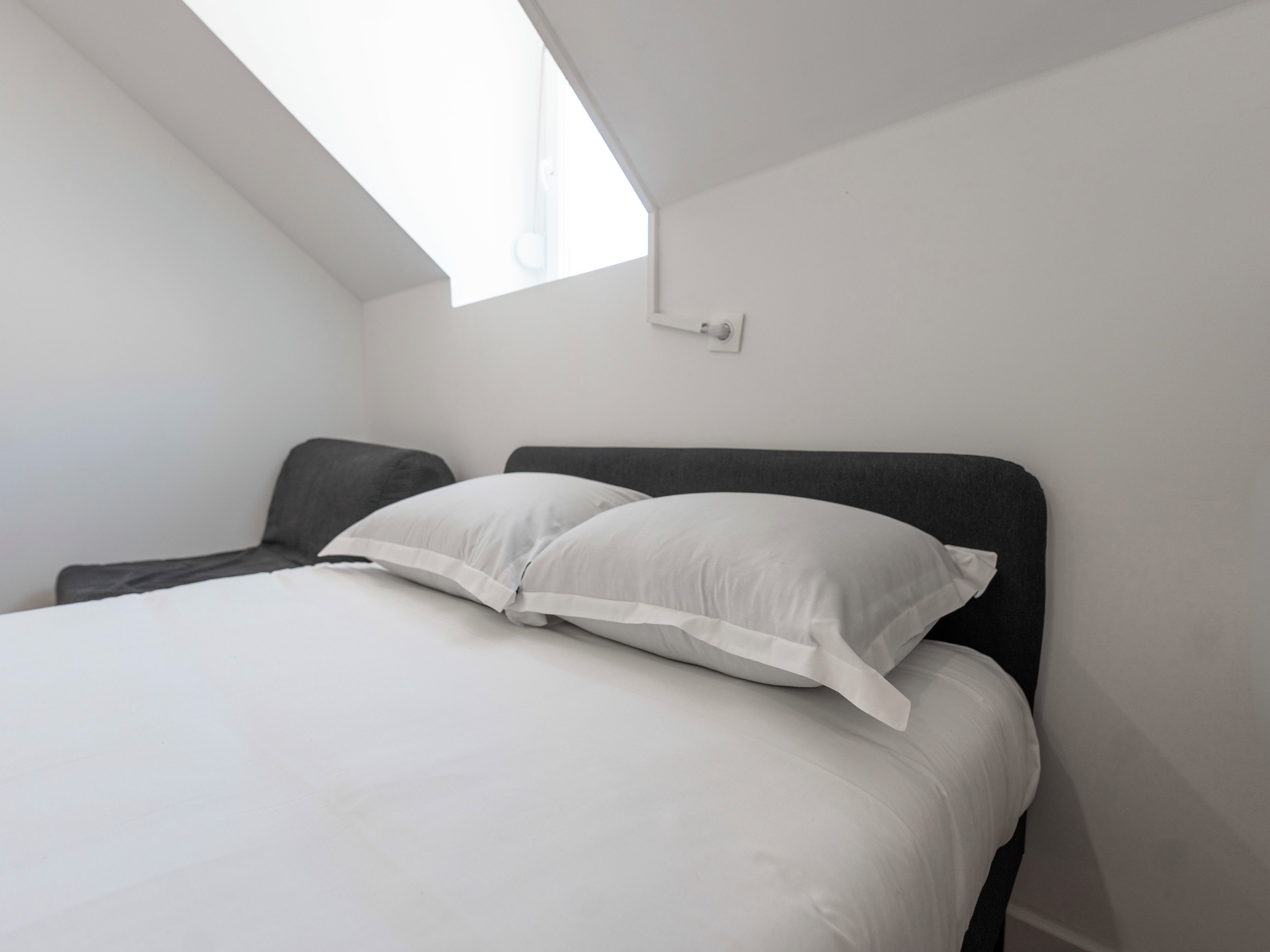 A bedroom with a bed, a window, and a wall-mounted light fixture.