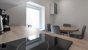 A modern kitchen with a built-in coffee machine, a dining area with a round table and four chairs, and a window providing natural light. - #IR | L'Amiral 41 💟 - Grenoble (Grenoble)