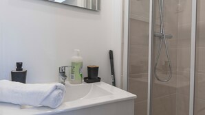 A bathroom with a white sink, a mirror, a towel, a bottle of liquid soap, and a shower head. - #IS | L'Amiral 42 💟 - Grenoble (Grenoble)
