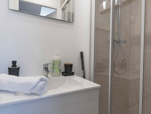Een badkamer met een wit wastafelmeubel, een spiegel, een handdoek, een fles handzeep en een douchekop.