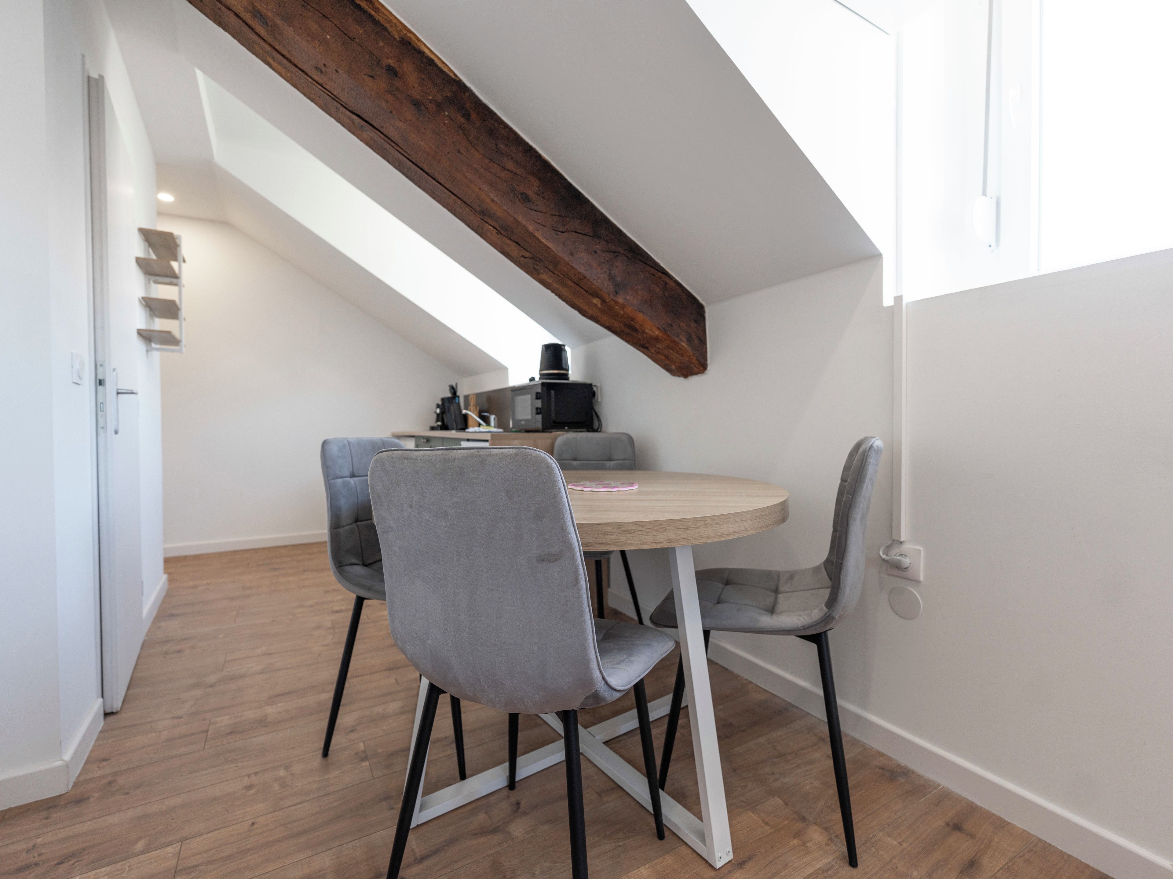 A dining area with a round table, four chairs, and a wooden beam ceiling.