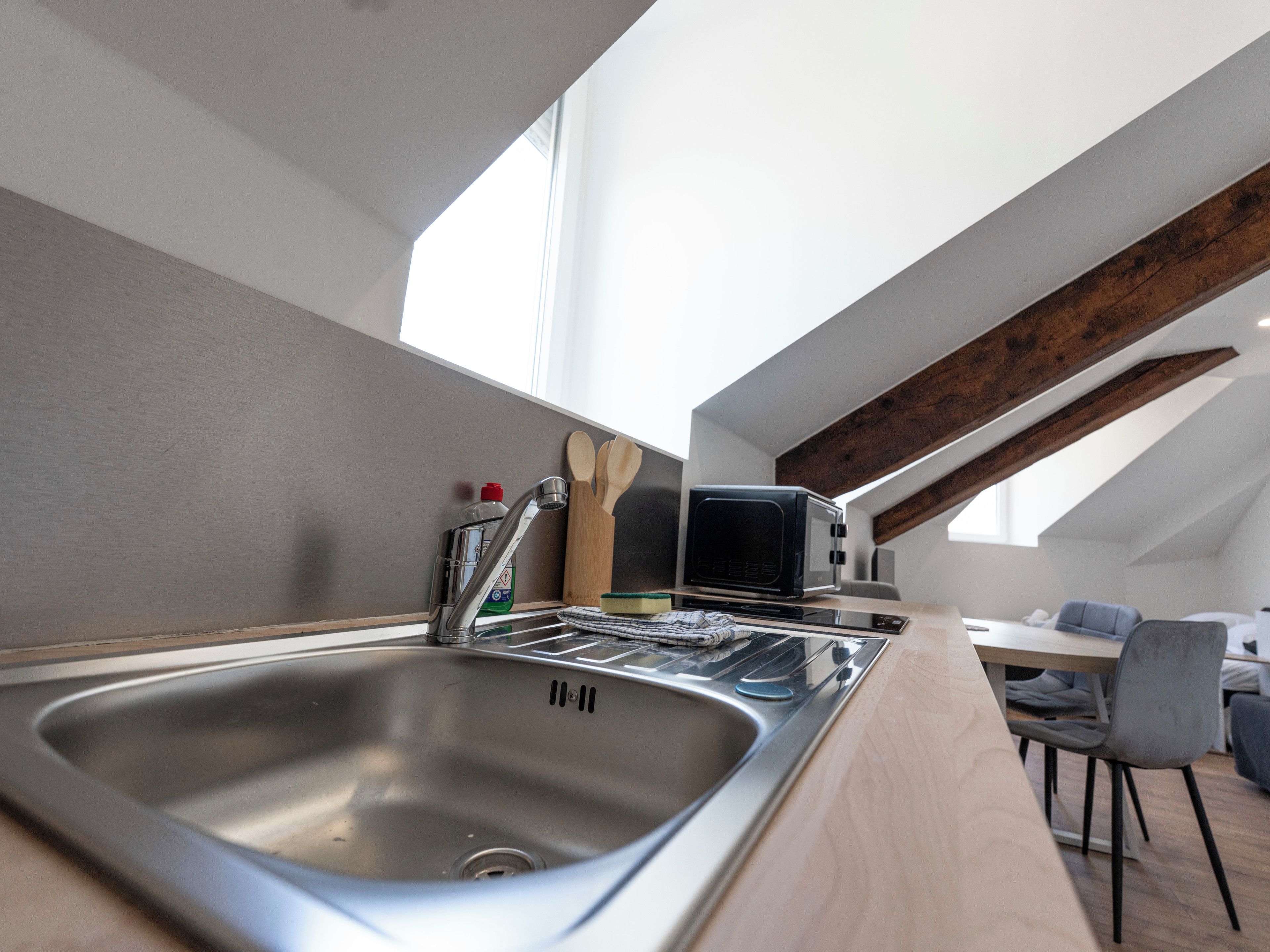 A modern kitchen with a stainless steel sink, a microwave, and wooden utensils on the counter.