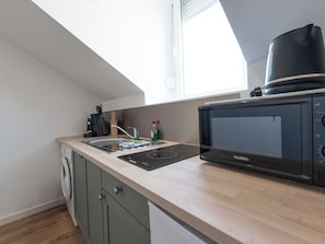 Een kleine keuken met een ingebouwde magnetron, een spoelbak en een wasmachine.