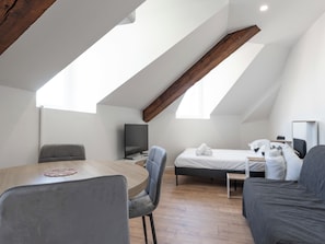 Een moderne, goed verlichte kamer met schuine plafonds, een bed, een bureau en een televisie.