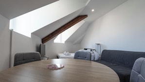 A modern loft bedroom with a sloped ceiling, a round dining table, a sofa, and a television. - #IS | L'Amiral 42 💟 - Grenoble (Grenoble)