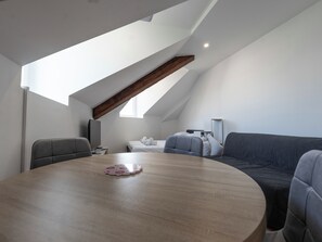 Een moderne loft slaapkamer met een schuine kap, een ronde eettafel, een bank en een televisie.