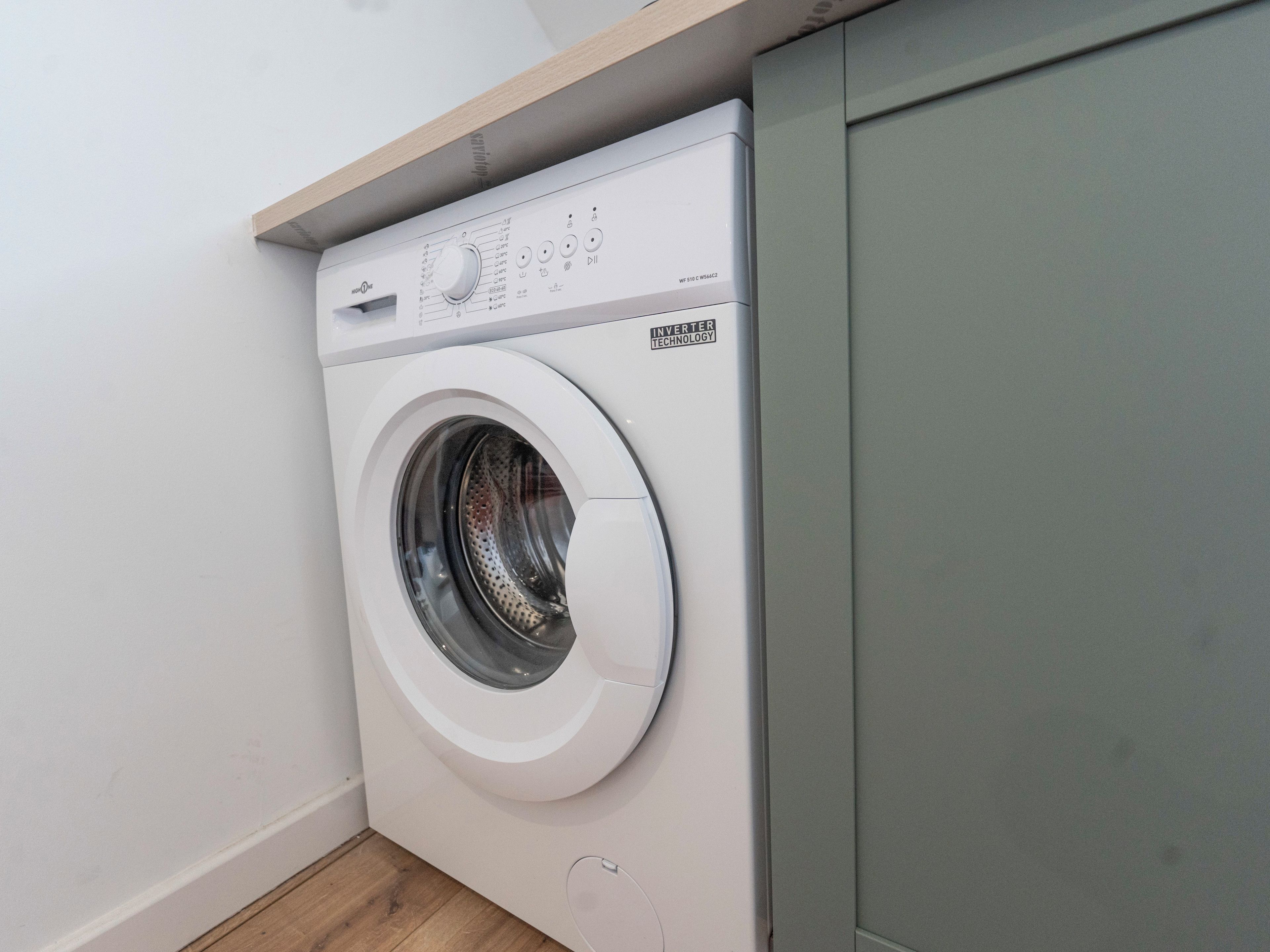 Een voorlader wasmachine met een bedieningspaneel, geplaatst in een hoek van een kamer met een houten plank erboven.