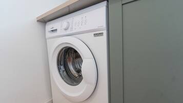 Een voorlader wasmachine met een bedieningspaneel, geplaatst in een hoek van een kamer met een houten plank erboven.