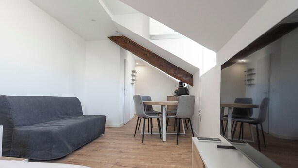 A modern, compact room with a sofa, a dining table with chairs, a large mirror, and a wooden ceiling beam. - #IS | L'Amiral 42 💟 - Grenoble (Grenoble)
