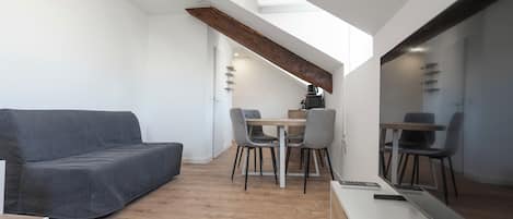 Una stanza moderna e funzionale con un divano, un tavolo da pranzo con sedie, uno specchio grande e un trave in legno al soffitto.
